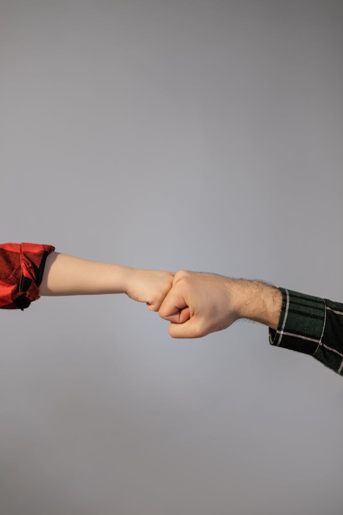 Close-up of an adult and child fist bumping against a neutral background.