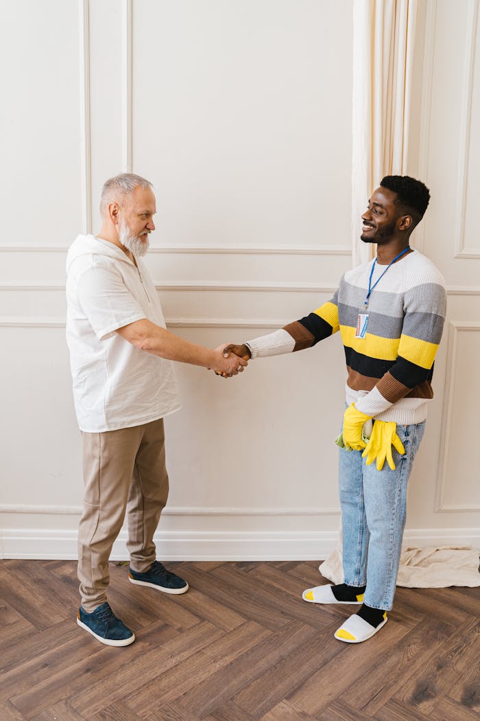 Two colleagues smiling and shaking hands indoors, representing cooperation and diversity.